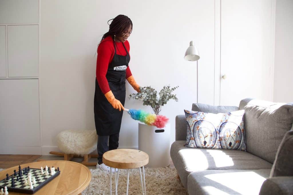 cleaning lady dusting a piece of furniture - airbnb cleaning checklist
