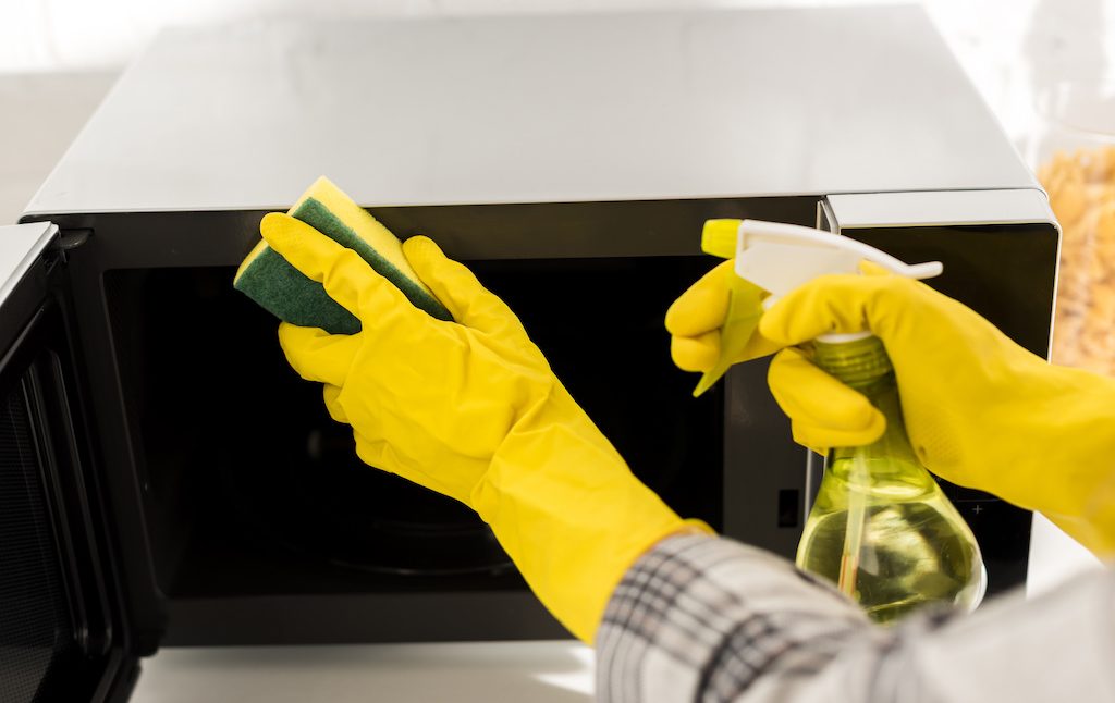 cropped view of woman in rubber gloves cleaning microwave with sponge