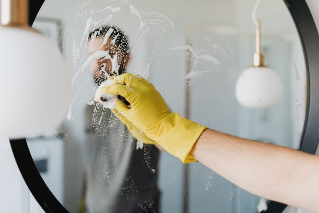 man cleaning mirror with yellow gloves- How to clean a mirror?