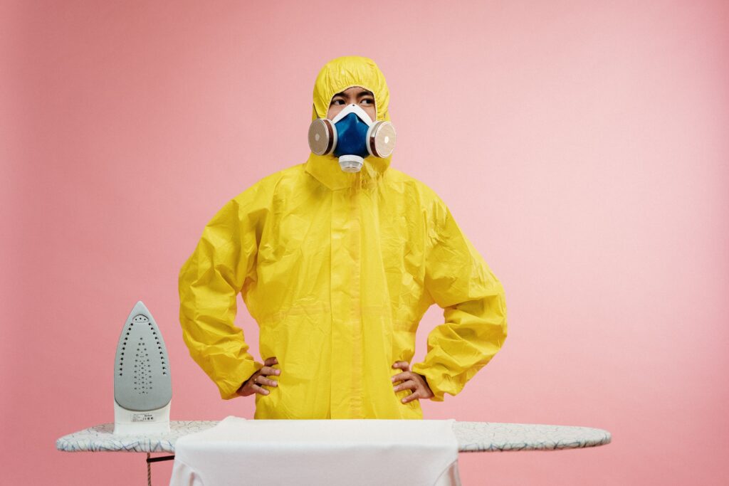 A man in overalls next to a table and an iron with clean clothes.