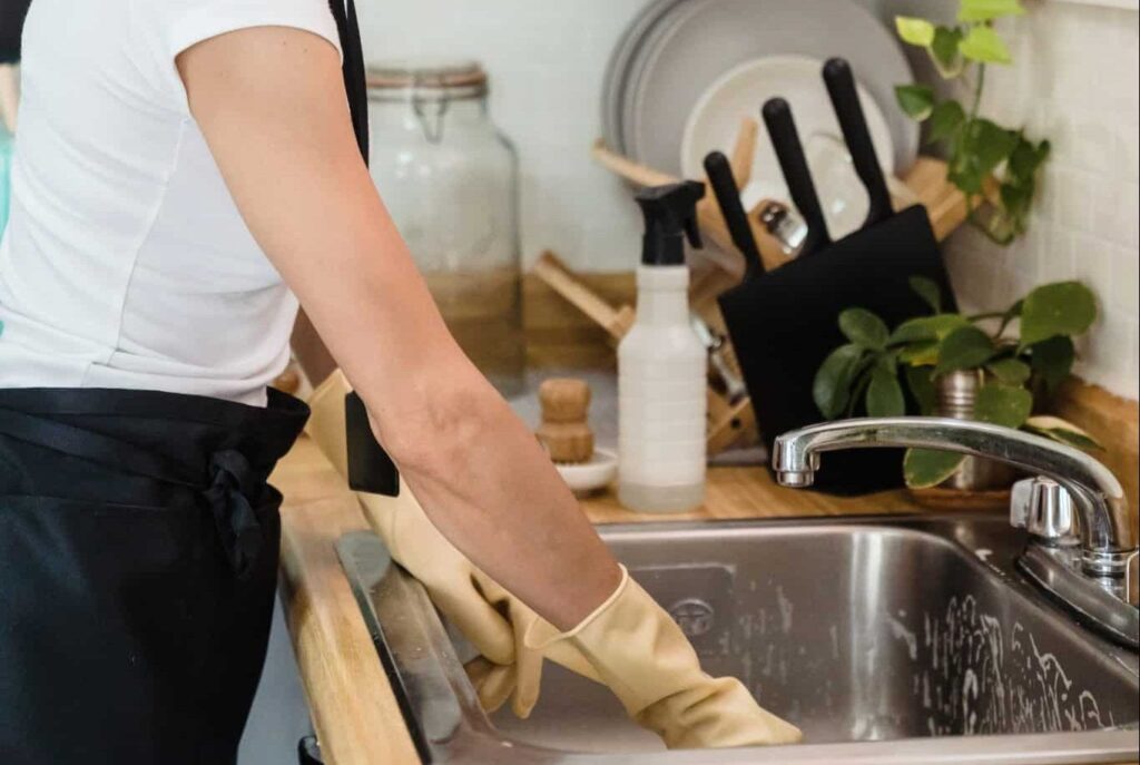 cleaning lady removing stains from a kitchen sink- How to Clean and Remove Stains from a Kitchen Sink - Expert Tips