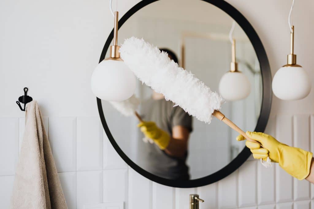 a lady running a feather duster over a mirror 