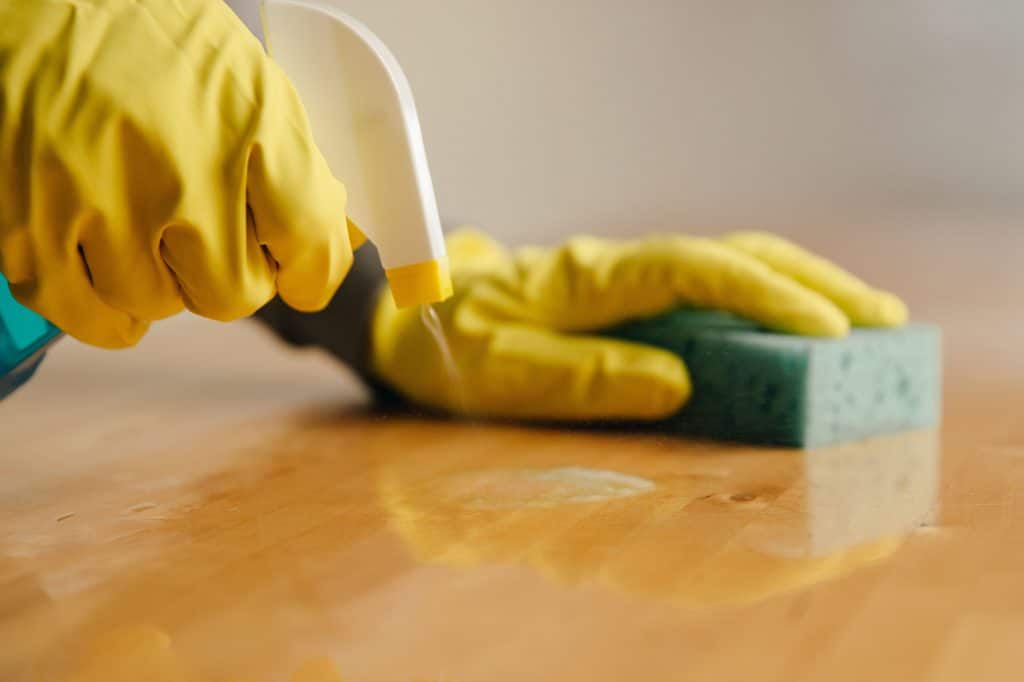 a cleaning spray in the right hand and a sponge in the other to clean a wooden surface.-office cleaning job