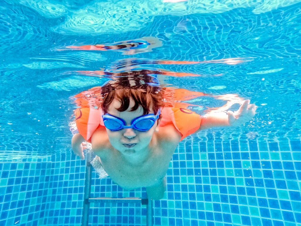 a boy in blue goggles swimming in a pool