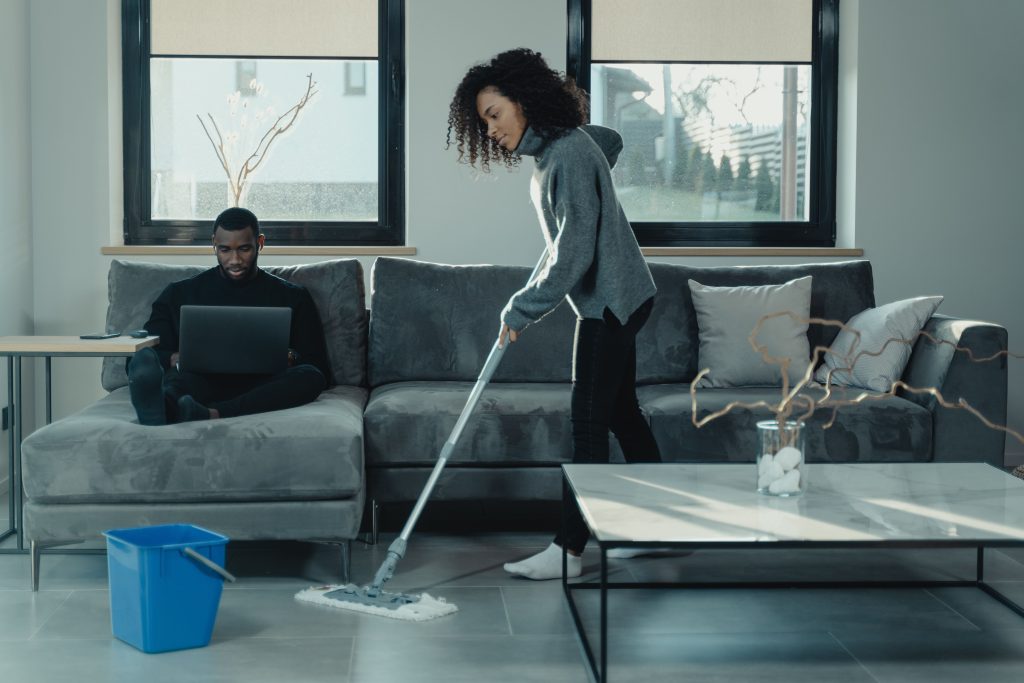 woman mopping the floor and man sitting on a gray couch-office cleaning job