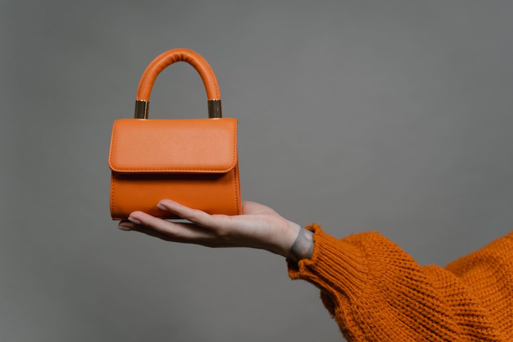 mini orange leather bag held by a person wearing knitted sweater-how to clean a leather handbag