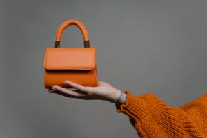 /mini-orange-leather-bag-held-by-a-person-wearing-knitted-sweater