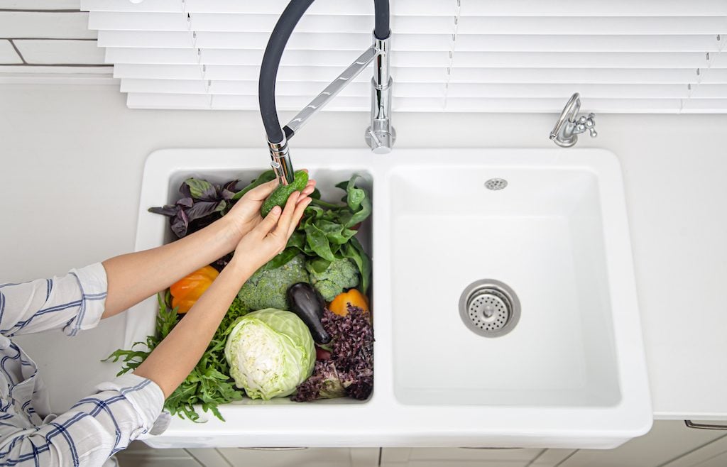 Female hands washing vegetables in the kitchen sink of modern kitchen top view.