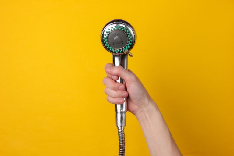 Hand holds a shower head on a yellow background.