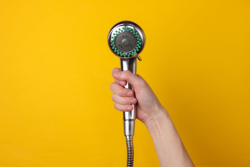 Hand holds a shower head on a yellow background.