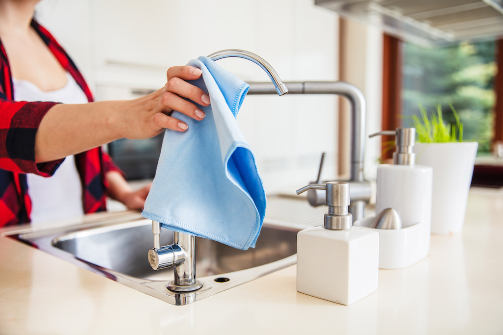 Woman is wiping the sink with blue cloth in the kitchen.