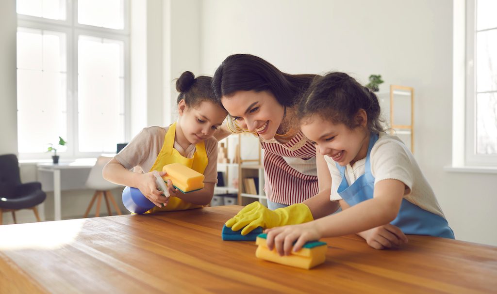sisters help their caring mother wash the kitchen table and clean the house