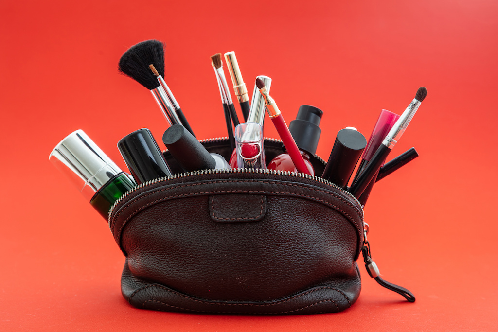 Makeup bag with cosmetics and makeup accessories against red background