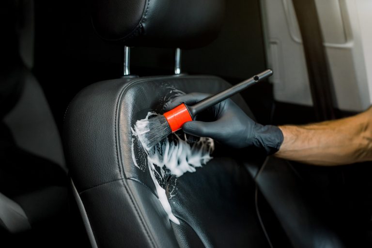 Young male worker cleaning car seat with foam and brush