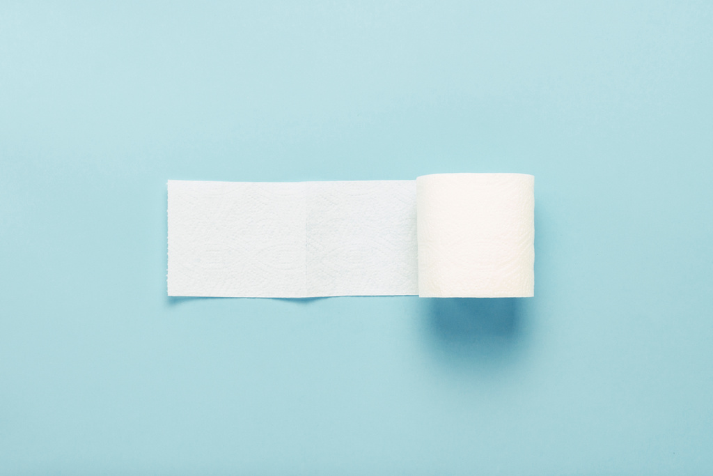 Roll of unfolded toilet paper on a blue background. Flat lay, top view