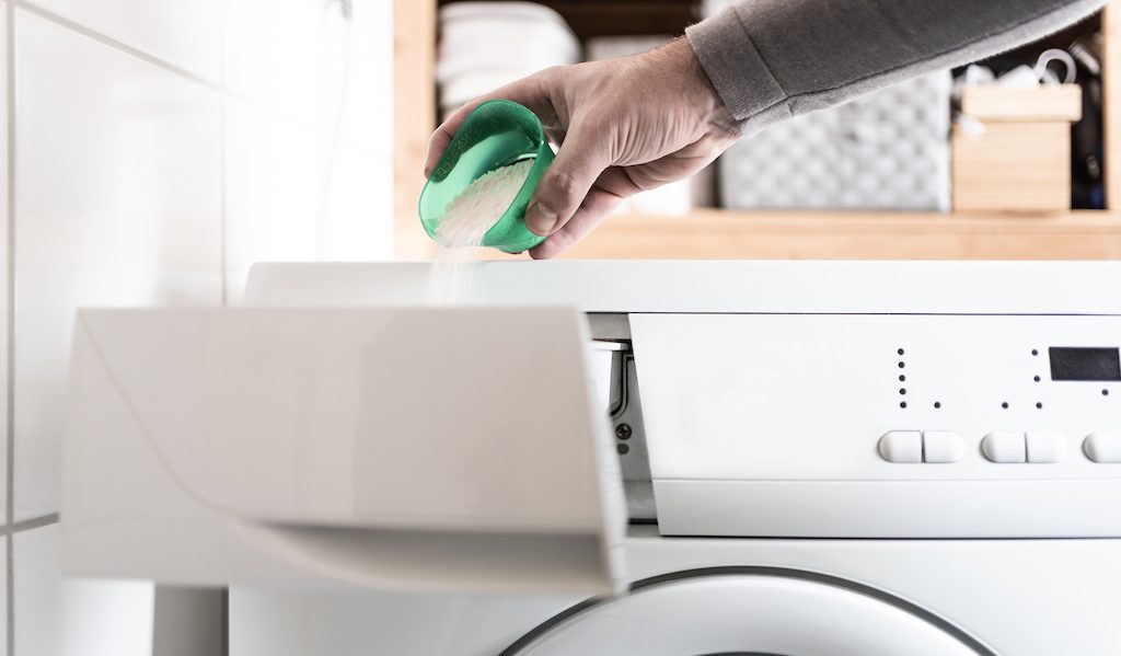 person using dosing aid to pout laundry detergent powder into washing machine